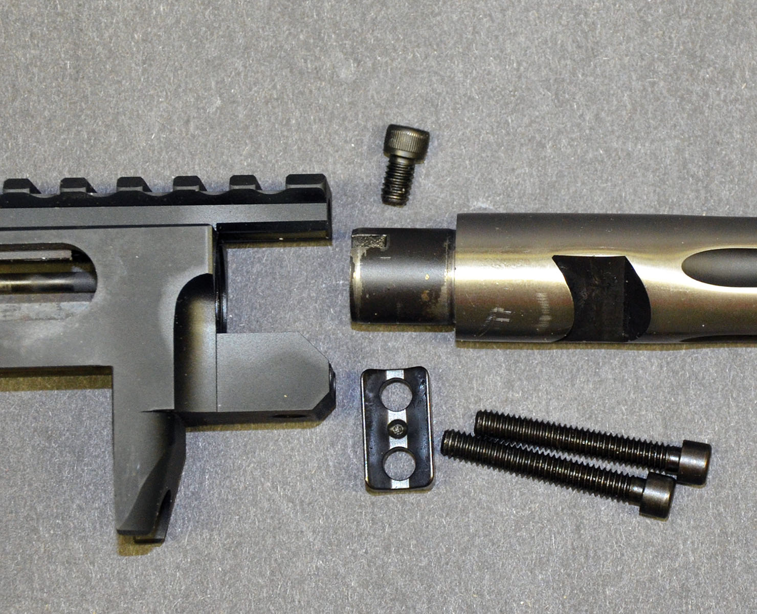 The aluminum 10/22 receiver was not designed to support a heavy barrel; and making the optic rail of the new Competition from Ruger’s Custom Shop an integral part of the receiver increased its rigidity. Equally important, it made room at the front of the receiver for the threaded hole of an additional upper barrel retainer screw. The screw is positioned parallel with the barrel and when tightened, the underside of its head bears on a small shoulder machined into the top of the barrel. Retention force is equalized by applying the same amount of force against the barrel as the V-block at the bottom of the barrel.